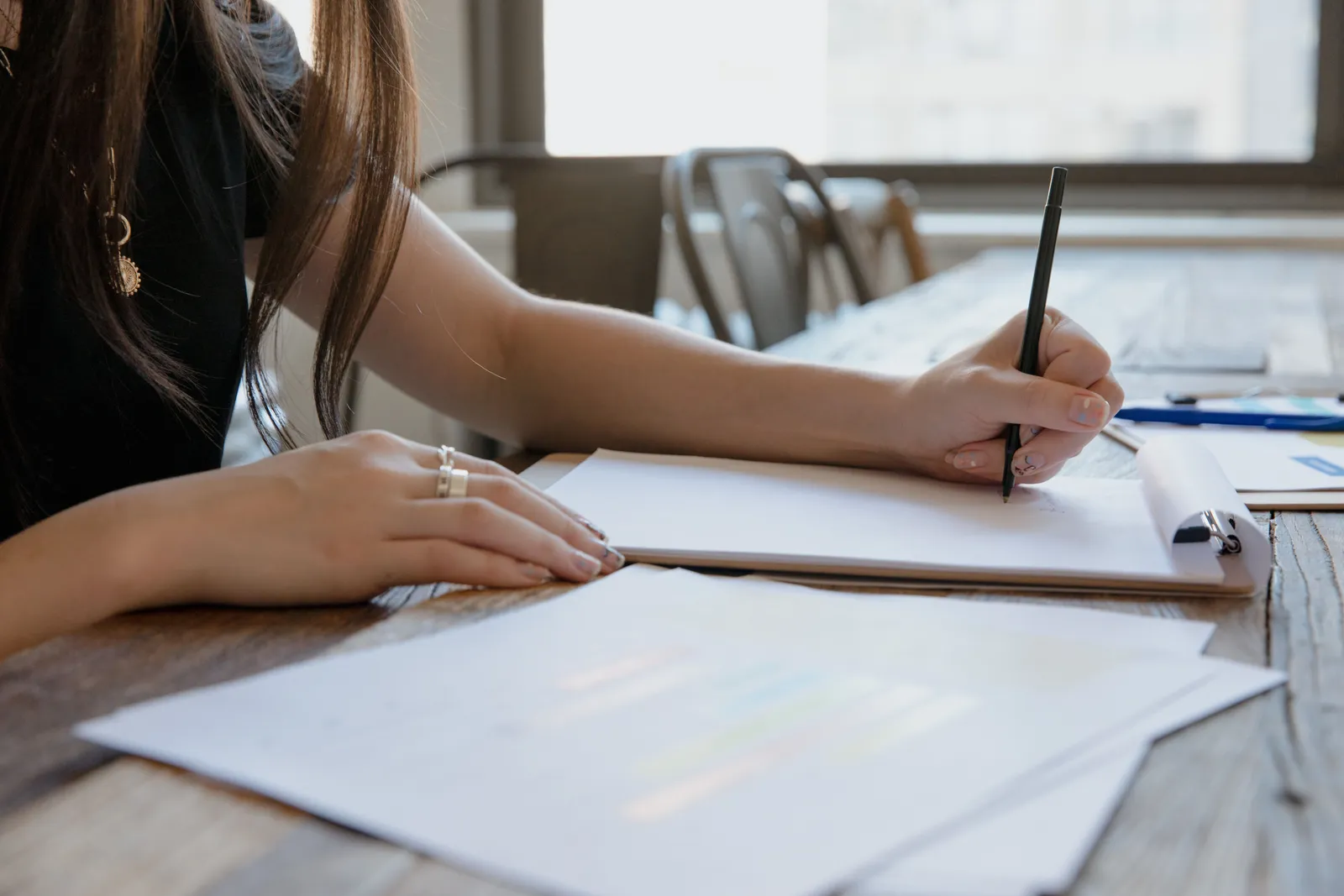 Close-up of a woman writing on paper at a wooden desk, indoors