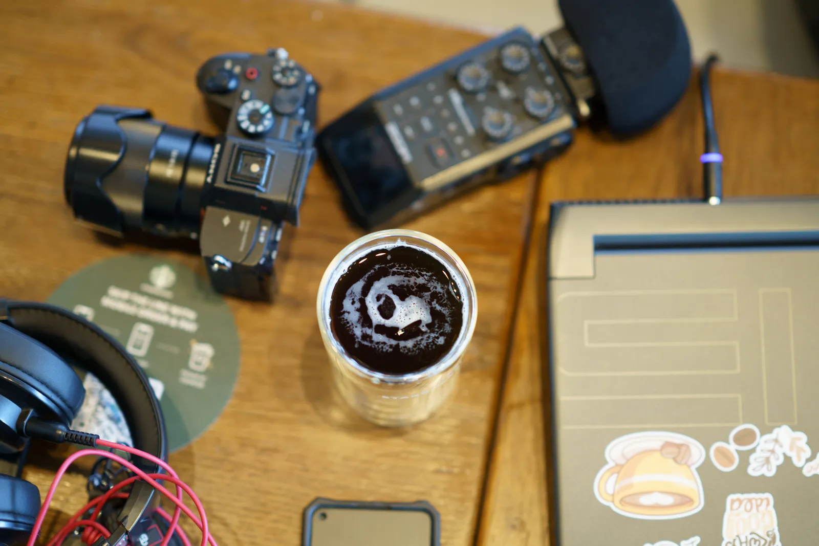 Overhead view of a workspace featuring a camera, headphones, audio gear, and a cup of coffee