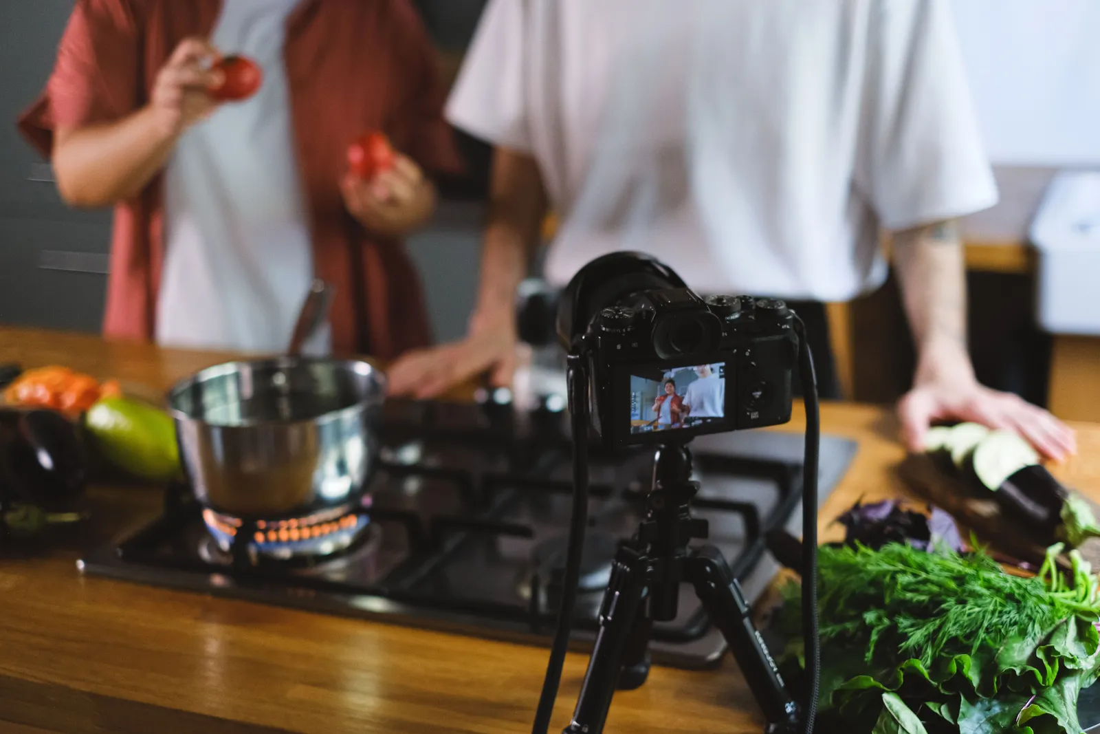 Two people filming a cooking video with fresh vegetables and a camera setup on tripod