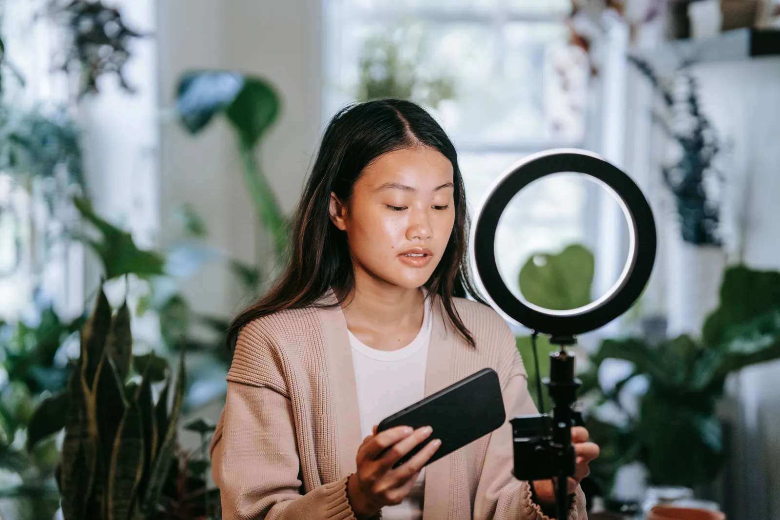 Woman adjusting smartphone and ring light indoors for video recording