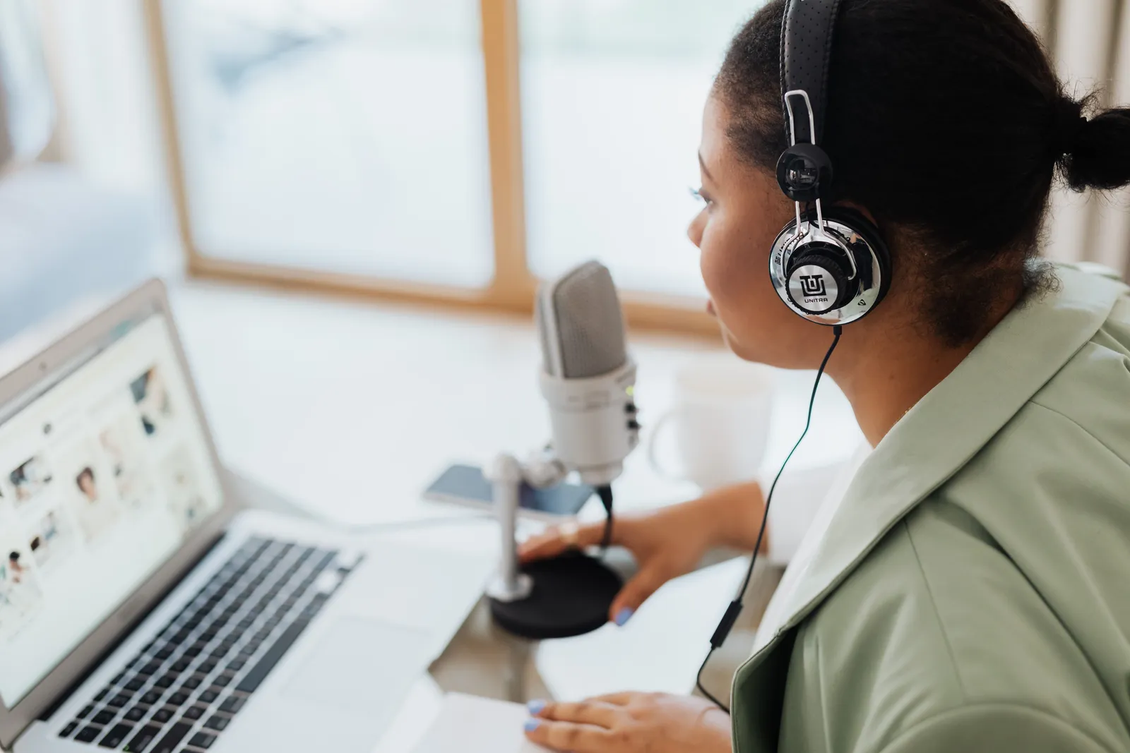 Woman wearing headphones recording podcast with laptop and microphone indoors