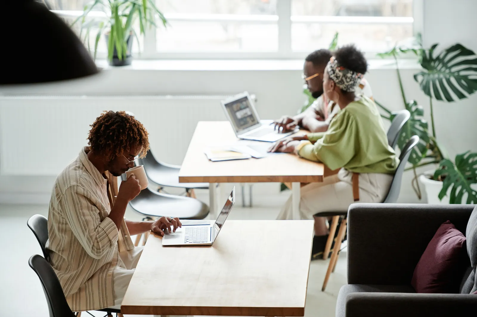 Diverse coworkers working in a modern office space with laptops and coffee, promoting teamwork and productivity