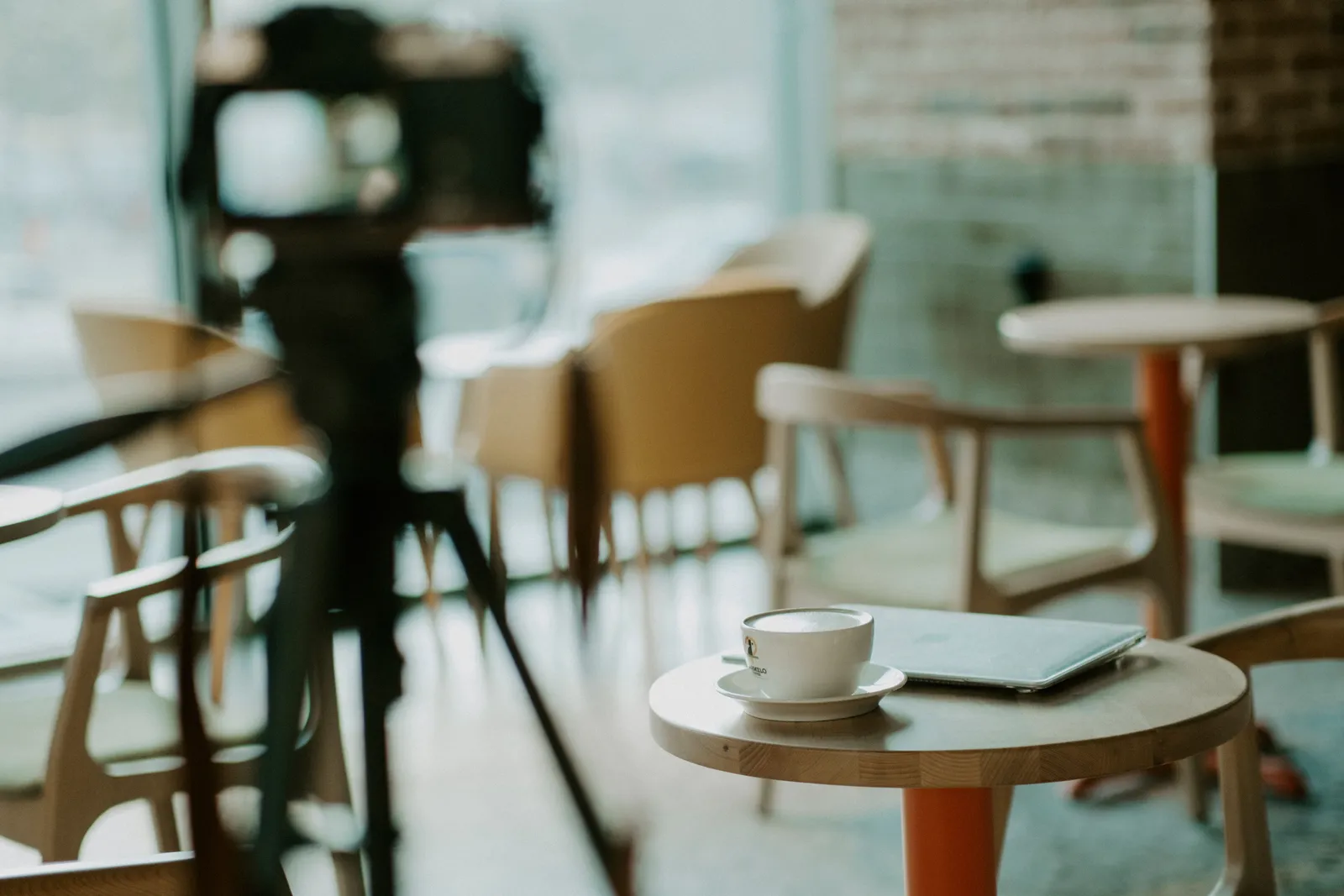 Warm café interior with coffee cup on table, laptop, and camera setup