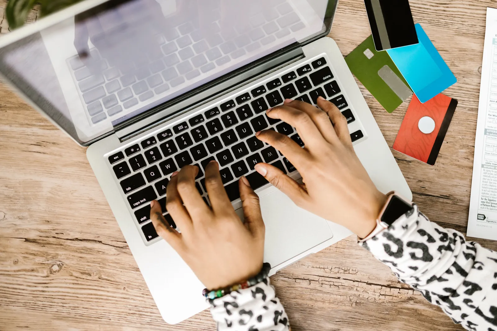 Person typing on a laptop with various credit cards on a wooden desk
