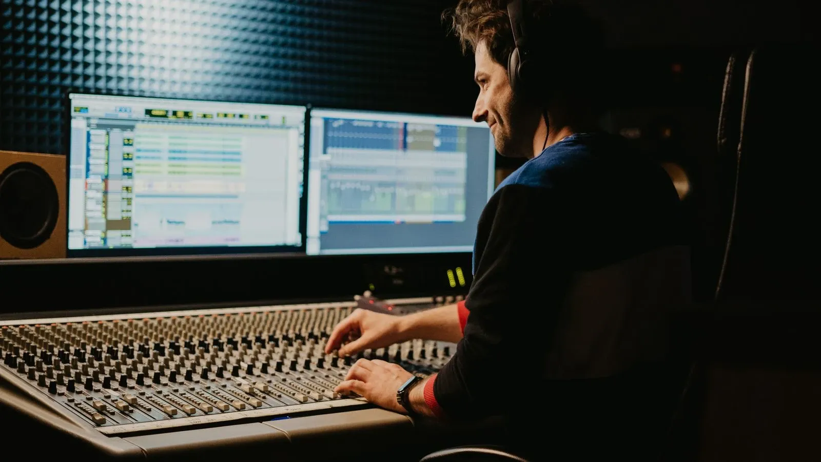 A sound engineer using headphones and adjusting a mixing console