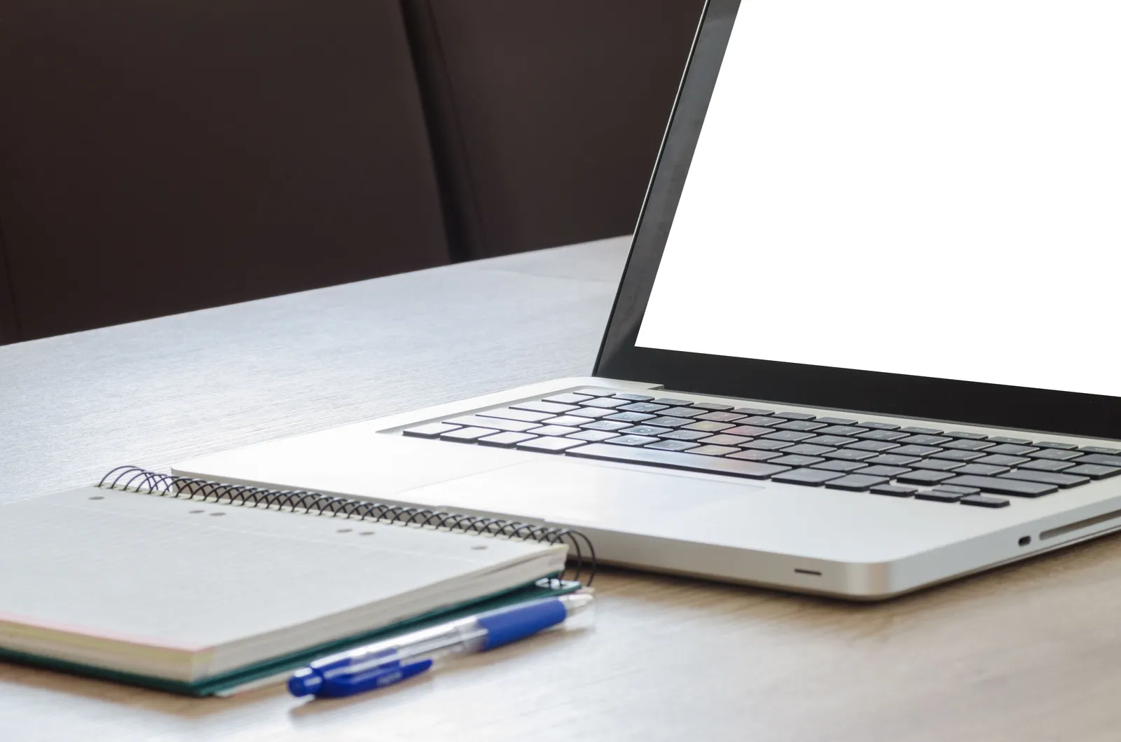 Open laptop with blank screen, notebook, and pen on a wooden desk, ideal for work or study
