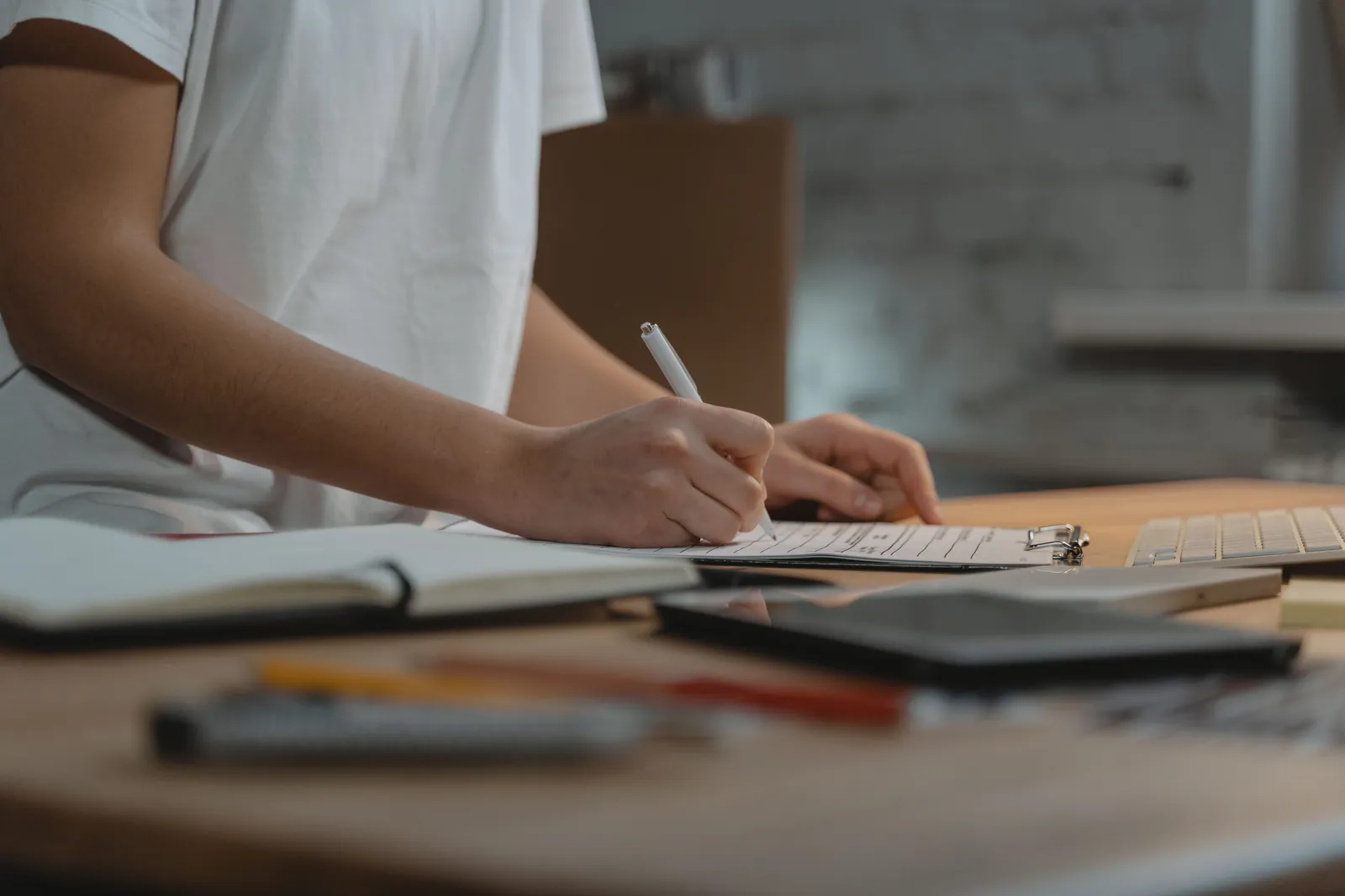 Close-up of individual writing on a clipboard at a desk with office supplies