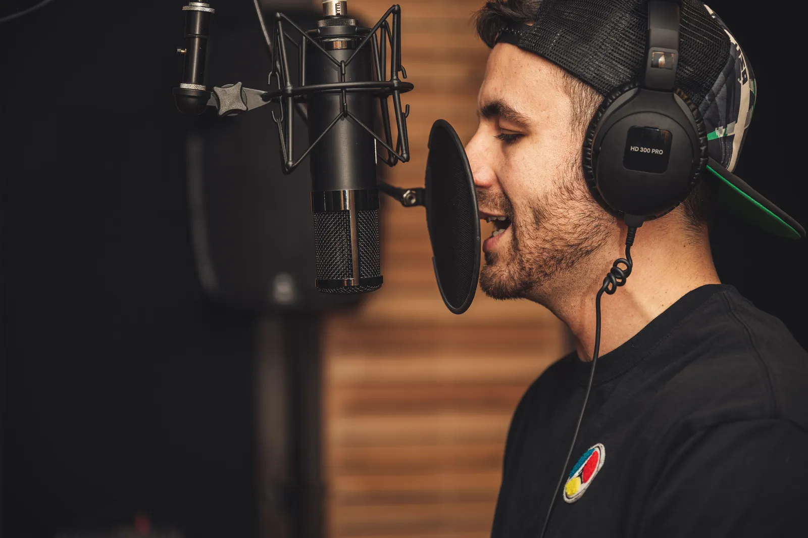 A young male musician singing in a professional recording studio with a microphone and headphones