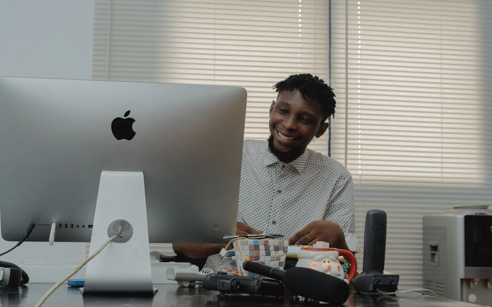 Man smiling while working at a desk with a computer in a well-lit office space