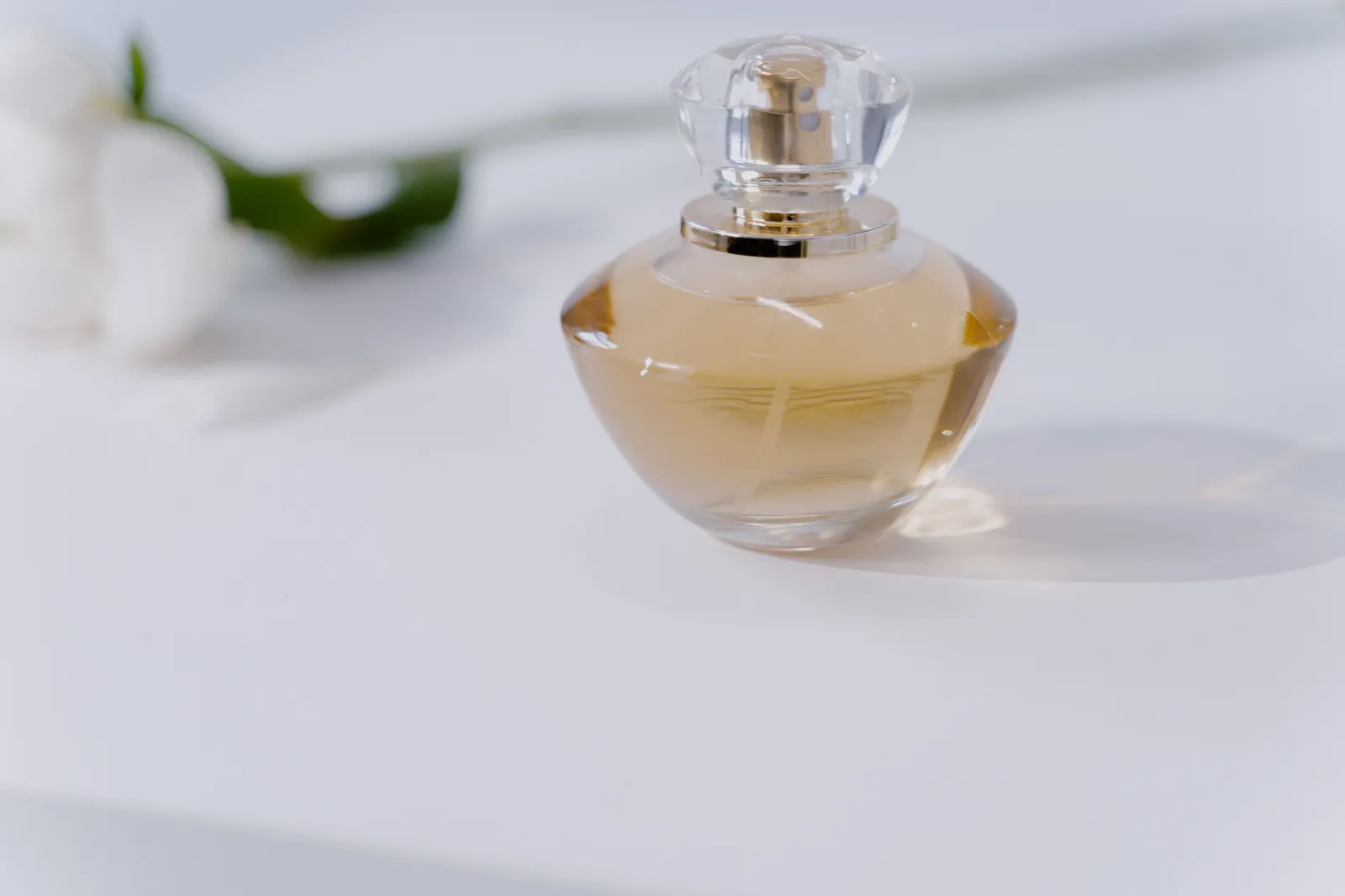 A clear perfume bottle with fragrance on a minimalist white table, exuding elegance