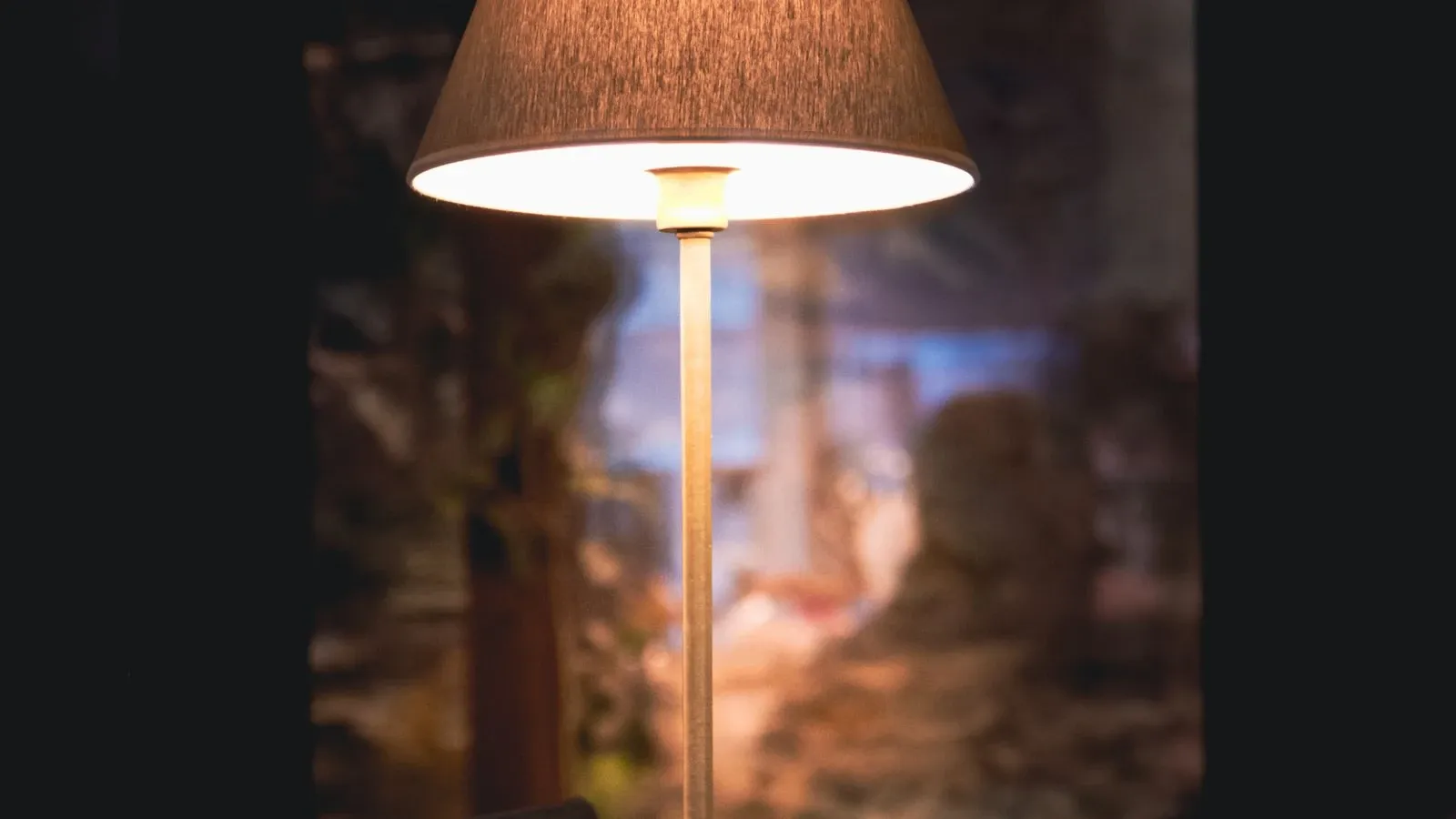 An illuminated lamp shade and slender stand against a dark background