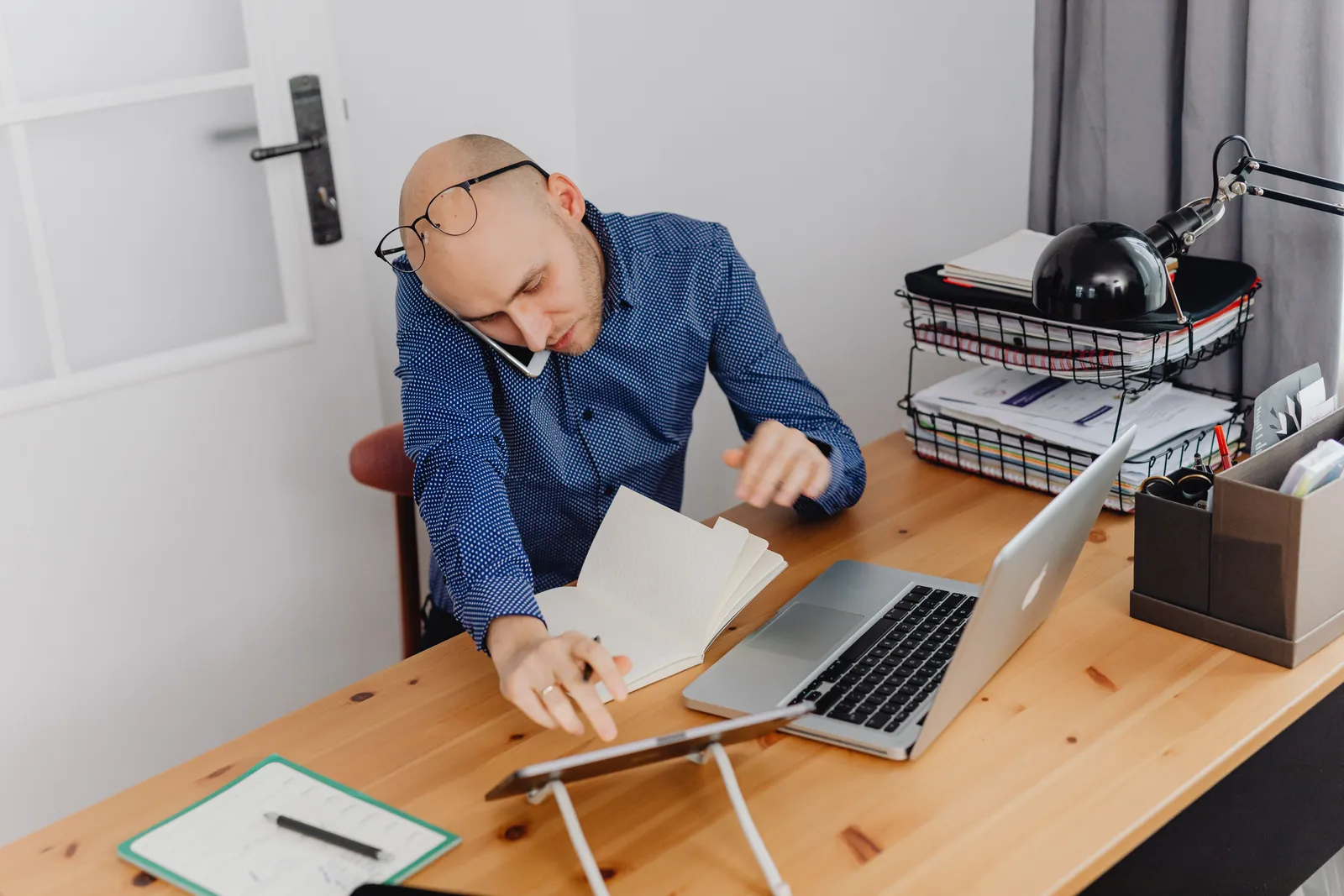 A man multitasking with phone, laptop, and notebook on his desk at home office
