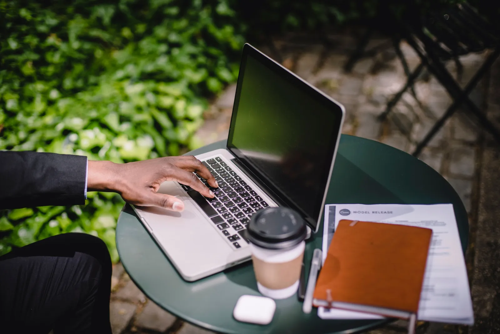 From above of crop faceless businessman typing on laptop keyboard while working remotely at round table with takeaway coffee