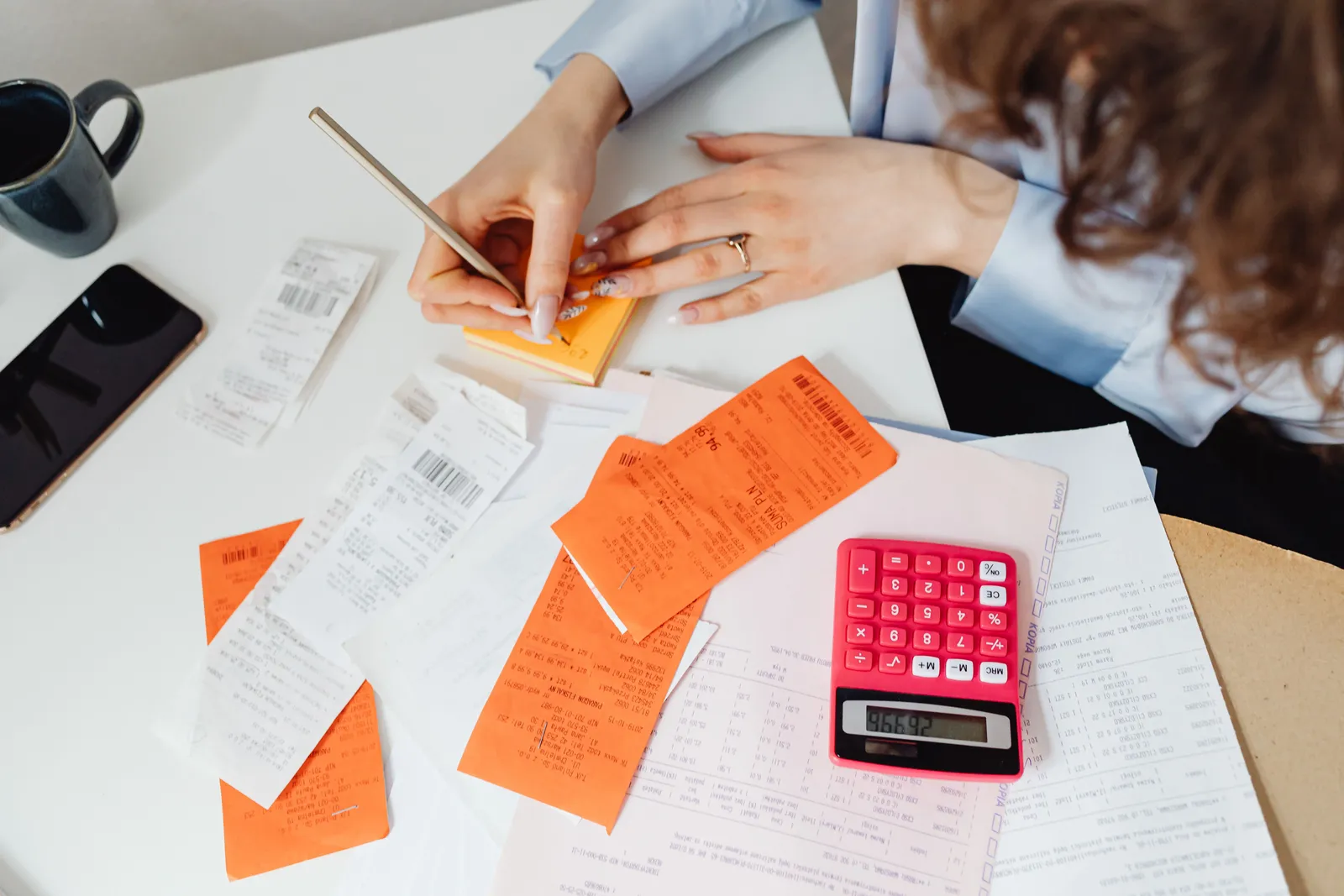 A woman writes down financial details using a calculator, receipts, and documents