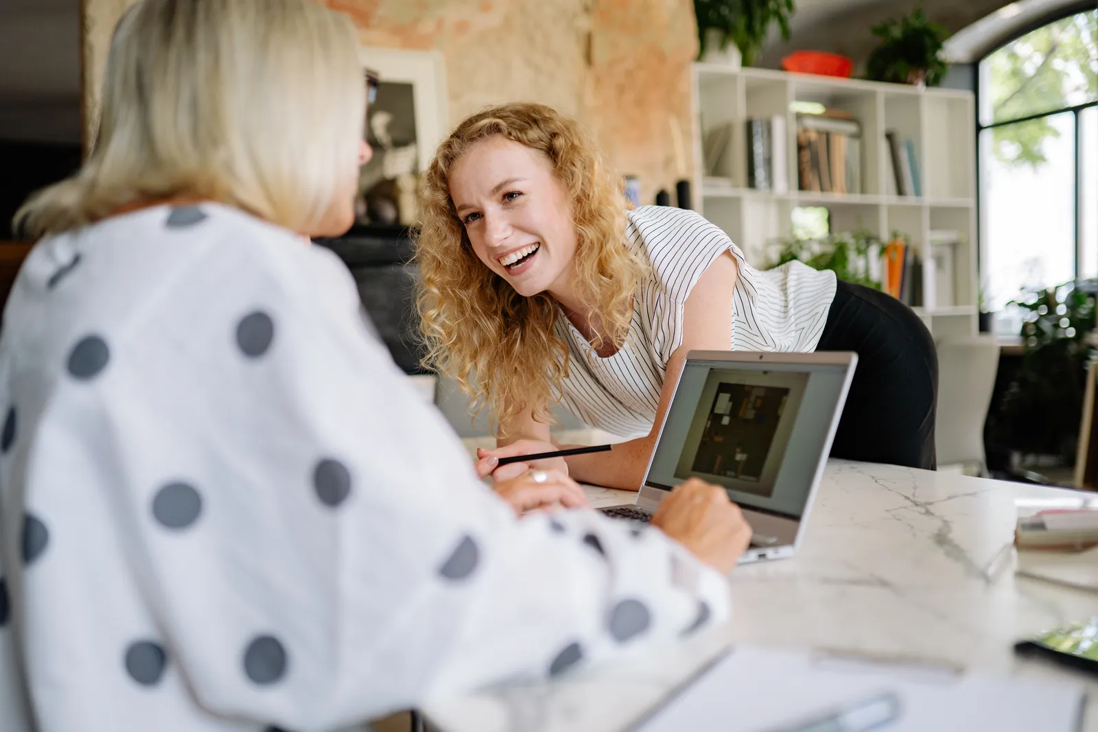 Two women at a desk, enjoying a light-hearted conversation and working on a laptop