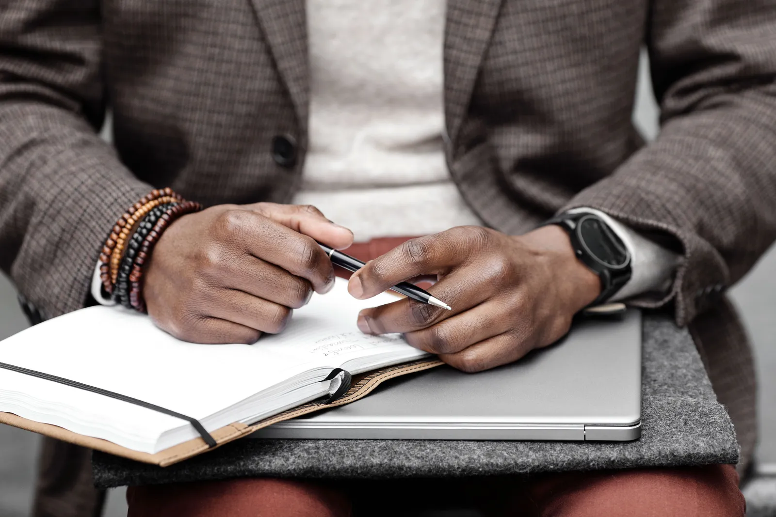 Close-up of a businessperson writing in a notebook on a laptop, dressed in smart casual attire