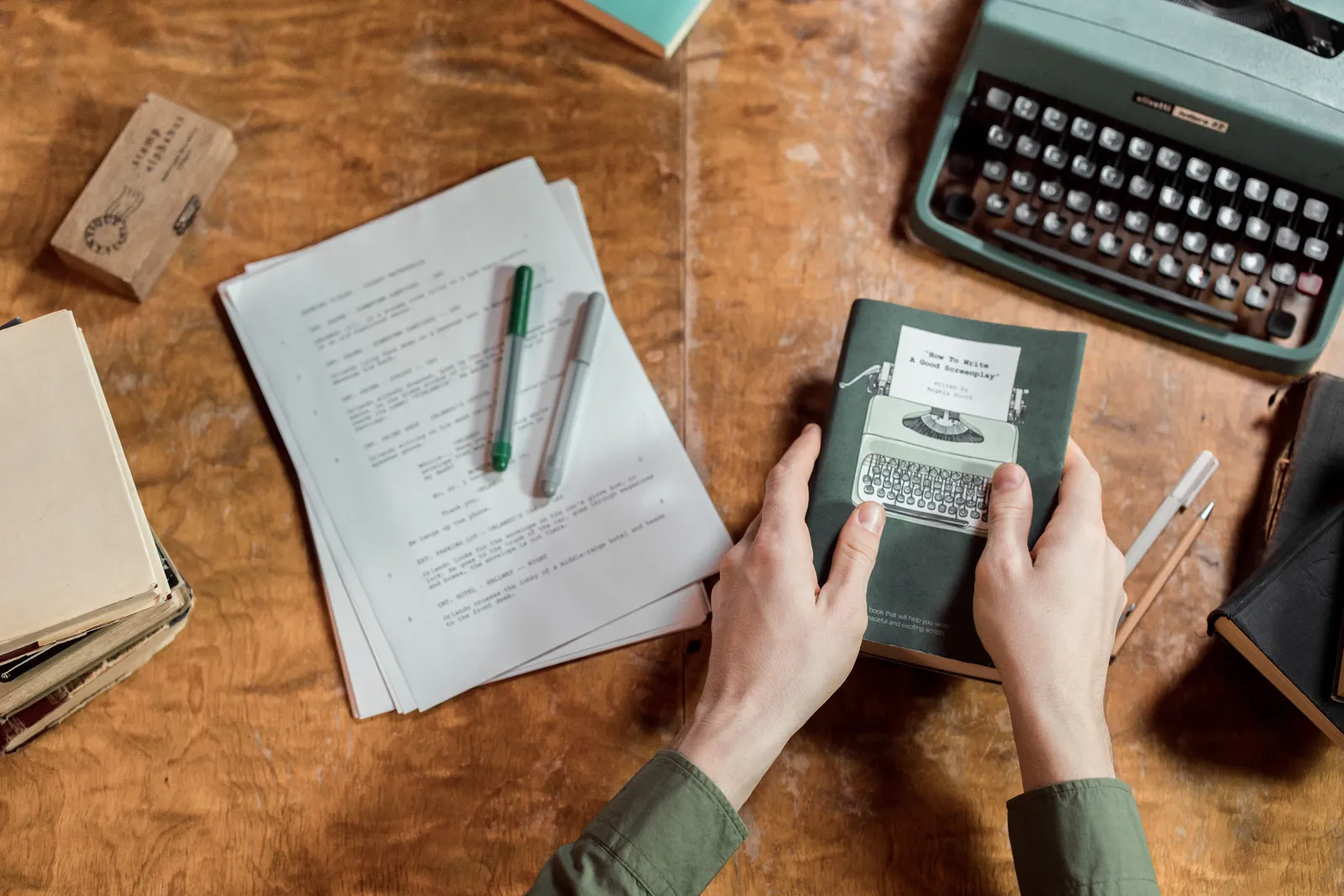 A vintage setup showcasing a typewriter, manuscripts, and hands holding a book on writing