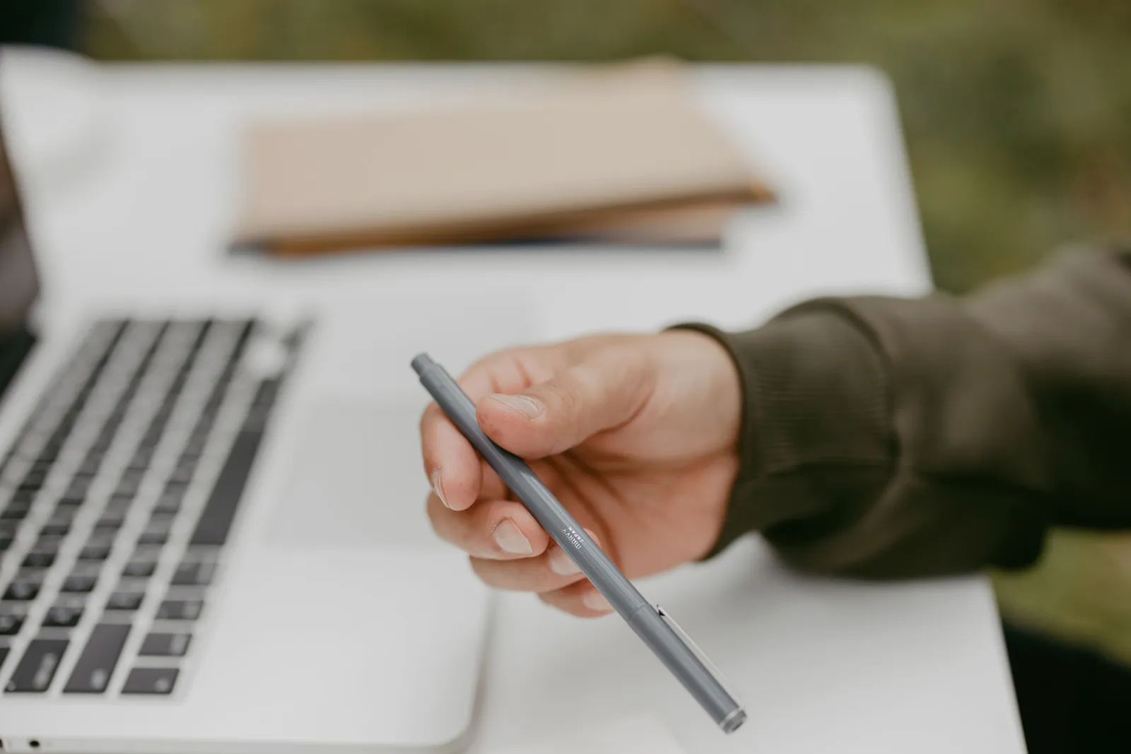Close-up of a person holding a ballpoint pen near a laptop, symbolizing work or study