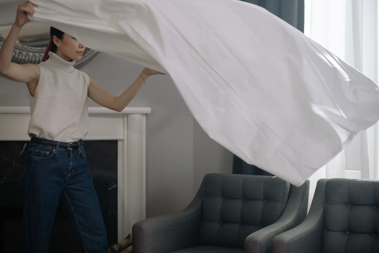 An woman shakes out a white sheet indoors, showcasing modern lifestyle and fashion