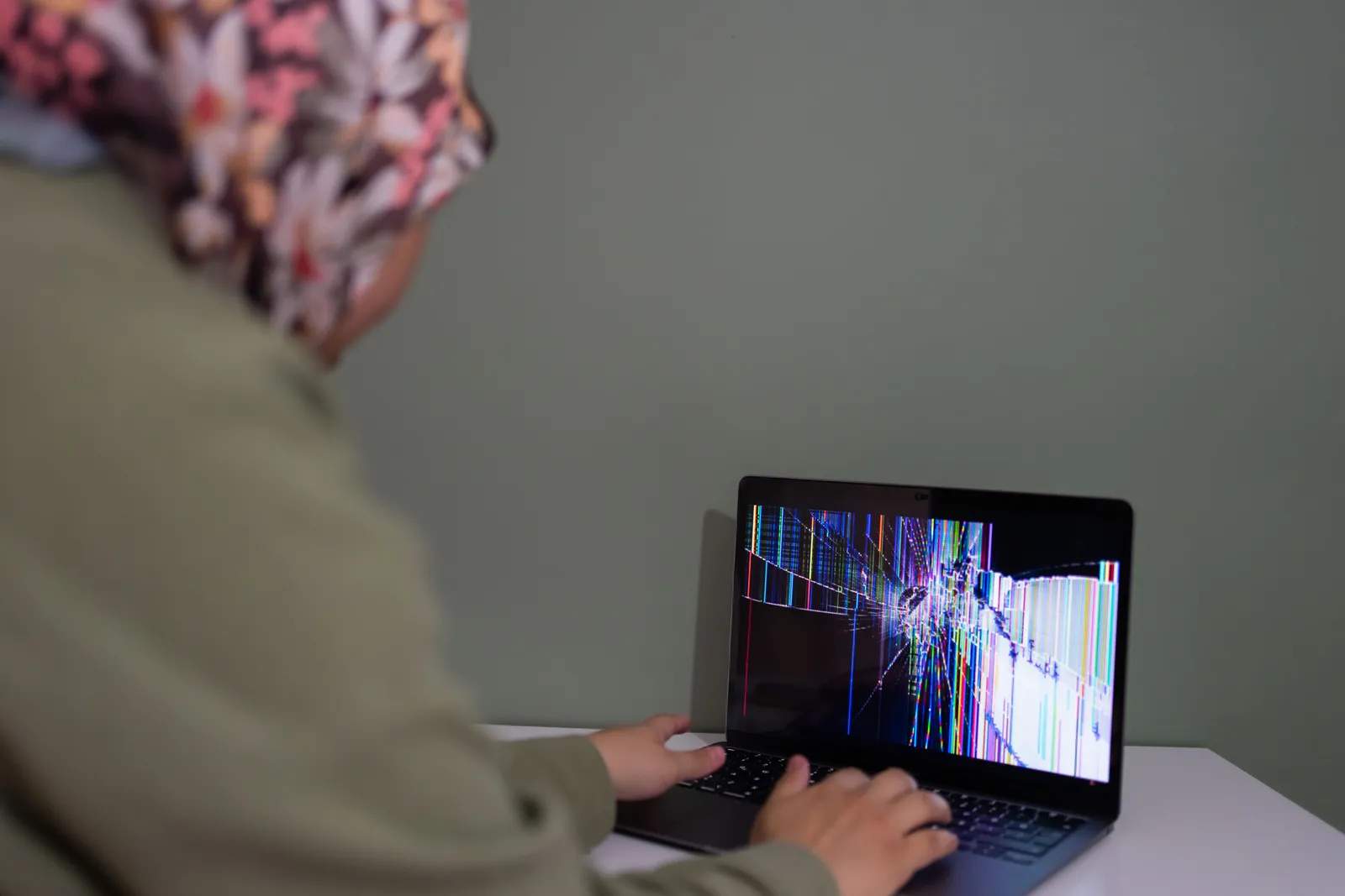 A person interacts with a laptop displaying a colorful cracked screen indoors