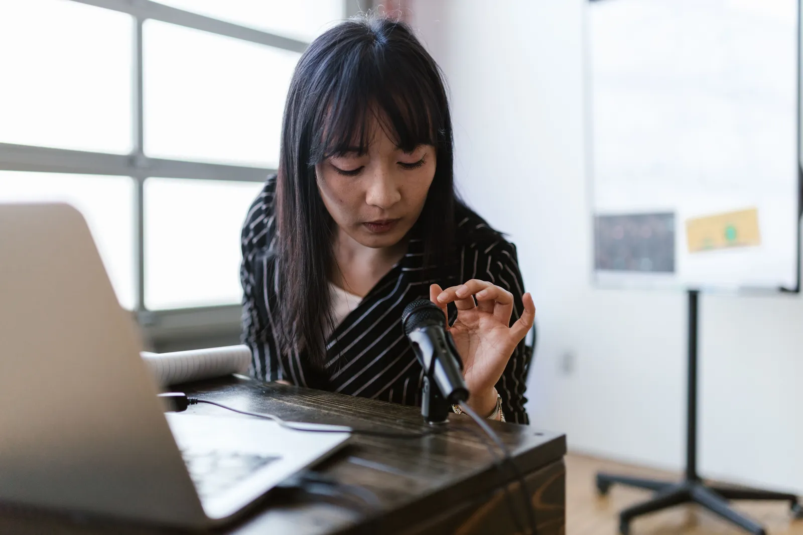 A woman in an office setting testing a microphone while sitting at a desk with a laptop