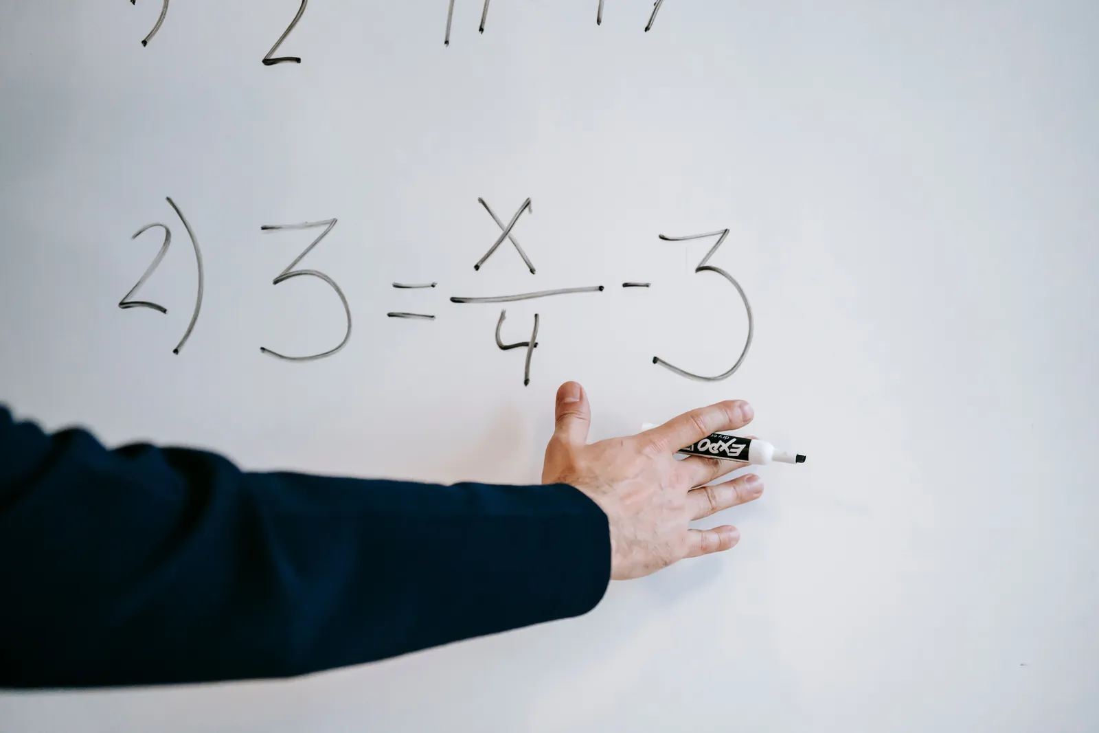 A hand writing a mathematical equation on a whiteboard with a marker