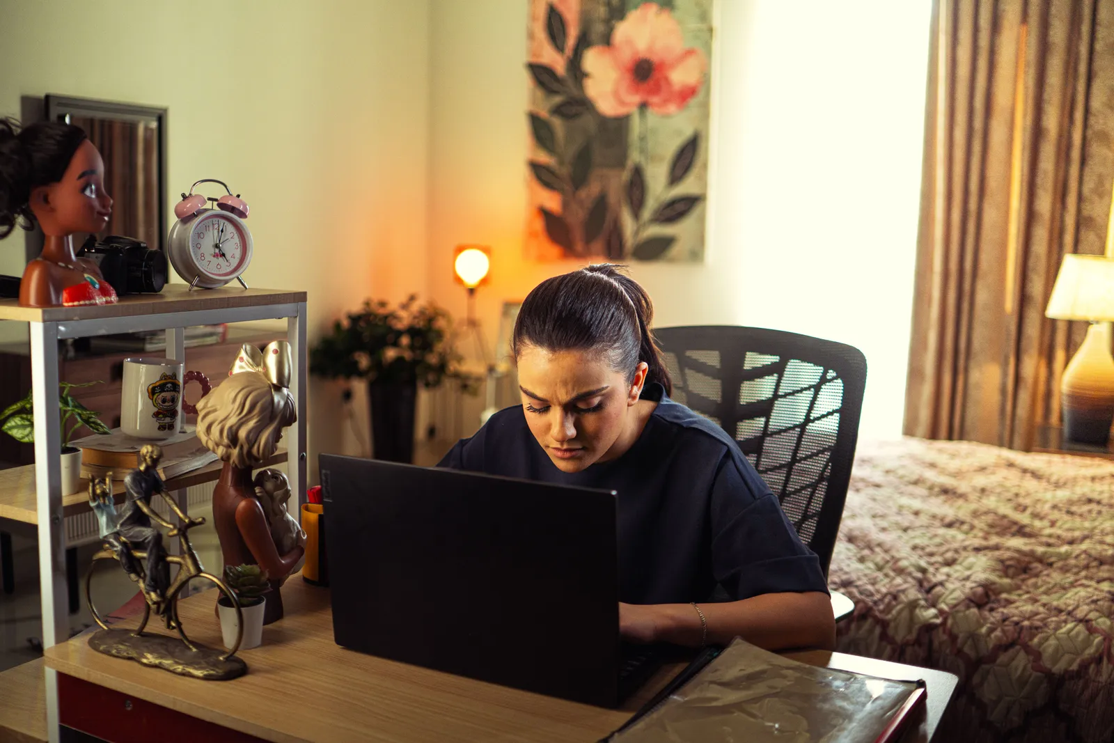 A woman intensely working on a laptop at her home office desk, surrounded by decor