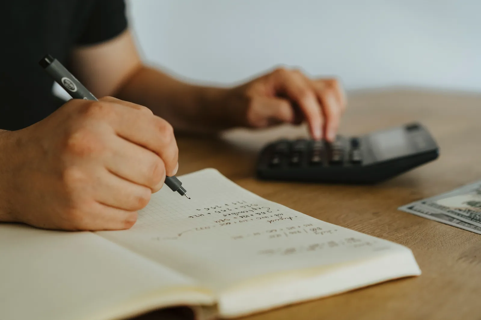 Close-up of hands writing calculations in a notebook with a calculator, focused on budgeting or financial work