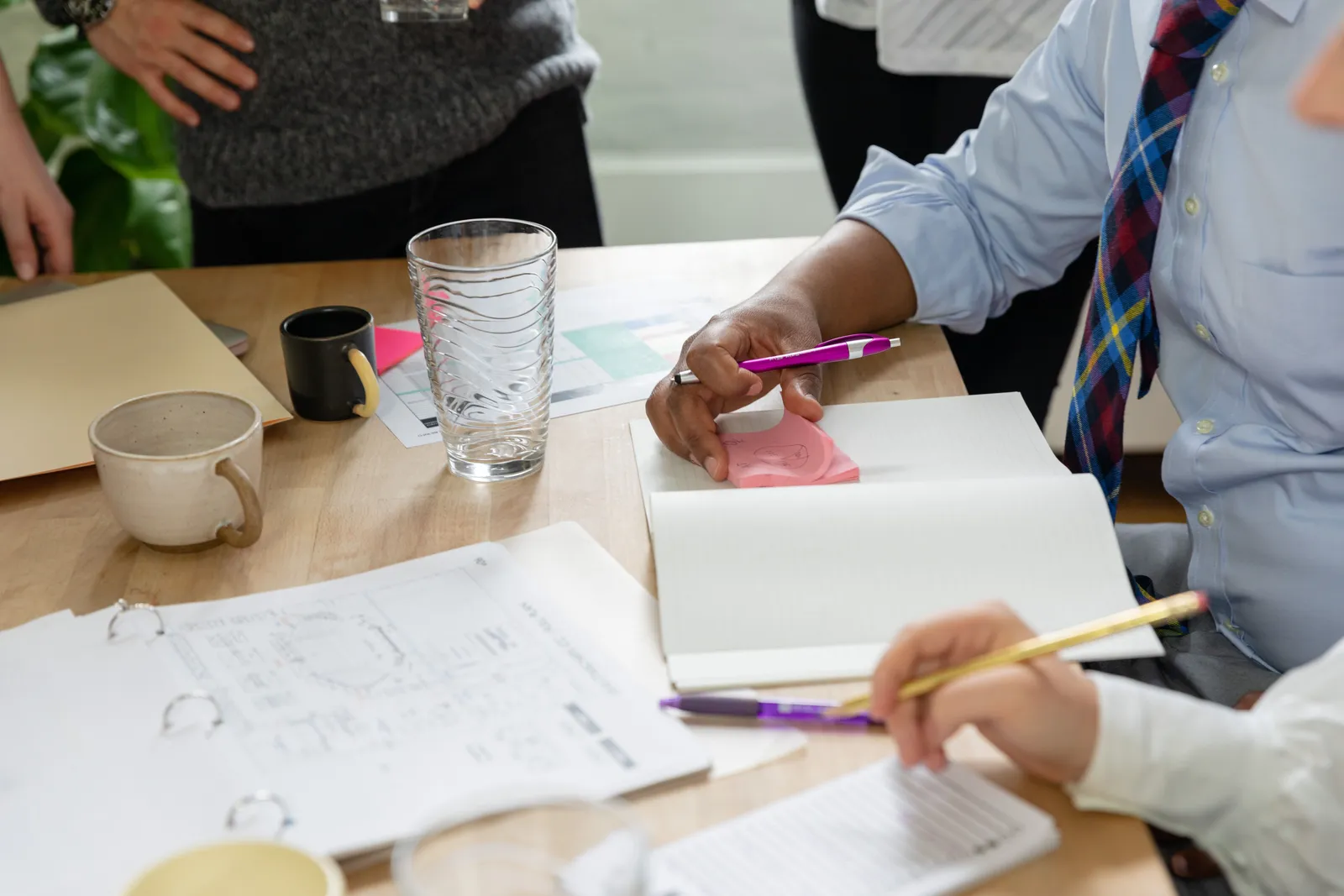 Business meeting with individuals taking notes on notebooks and discussing ideas at a wooden table