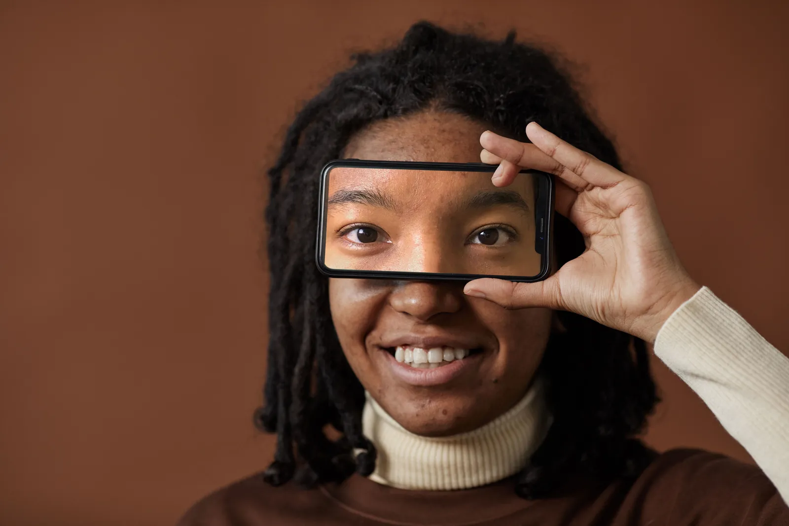 Woman smiling and holding smartphone to eyes in studio