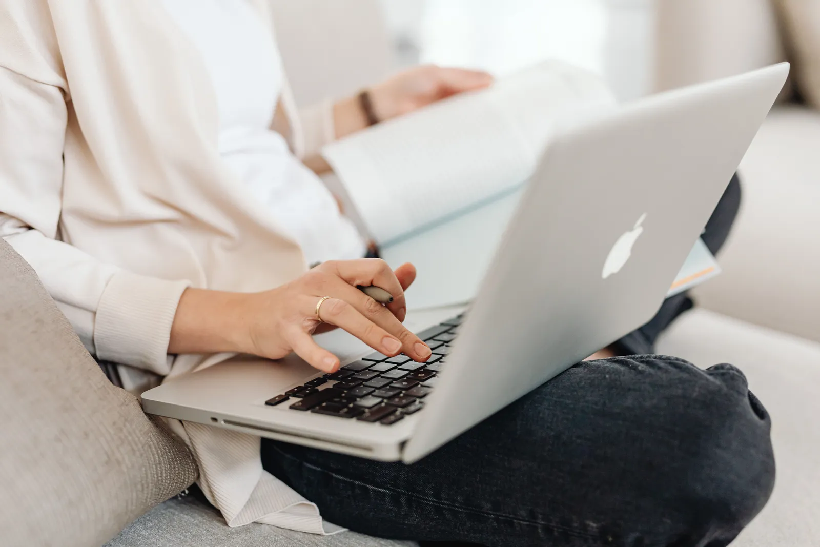 Close-up of a person multitasking, typing on a laptop while holding a book on their lap