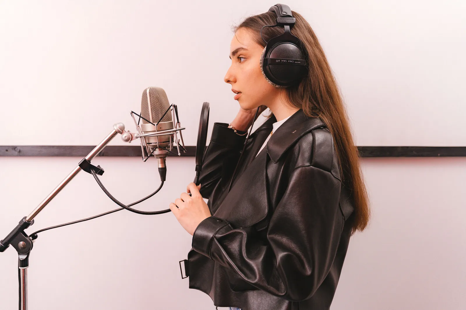 Young woman in leather jacket singing into microphone in studio setting