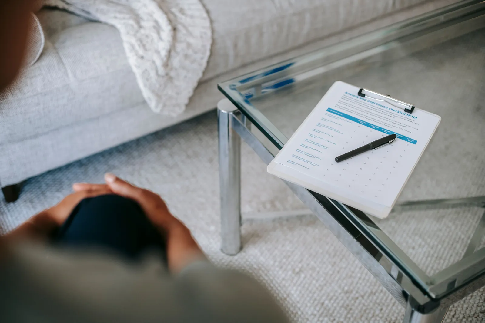 From above of blurred unrecognizable female psychologist sitting in office near table with clipboard and pen during session