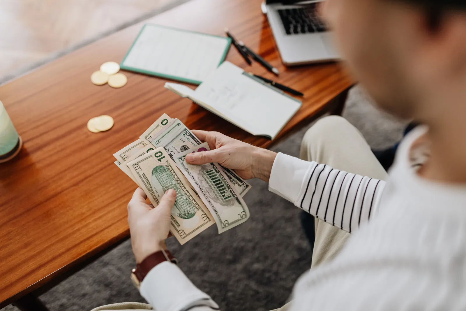 A person counts US dollar bills with a notebook and coins on the desk