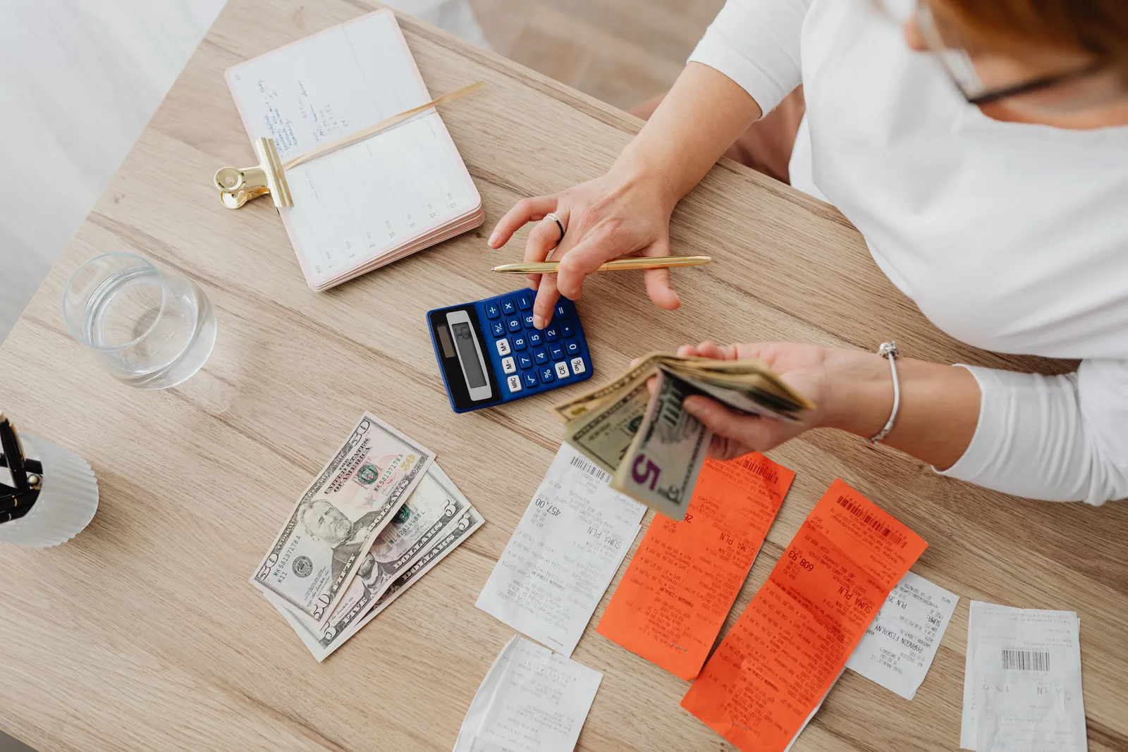 Overhead view of a person using a calculator to manage cash and receipts at a desk