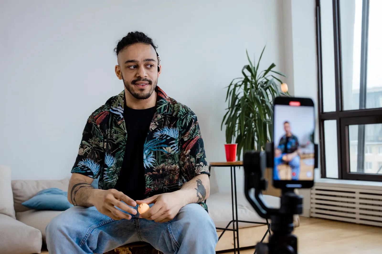 A young man recording video content indoors with a smartphone and tripod