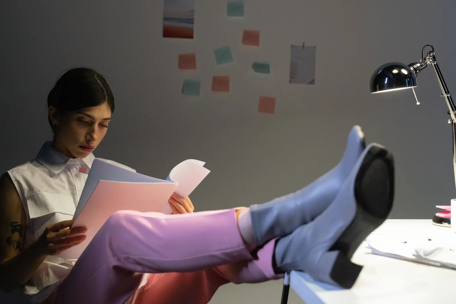 Woman in a modern office setting reading documents, feet up on desk under warm light