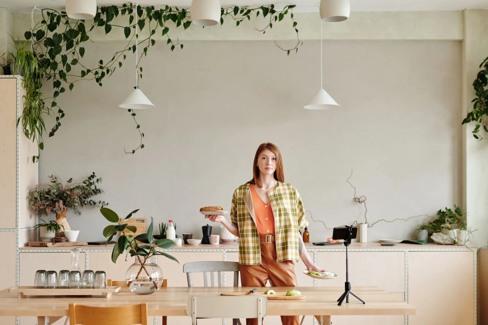 Woman in a modern kitchen setting up food for a vlog with a smartphone and tripod