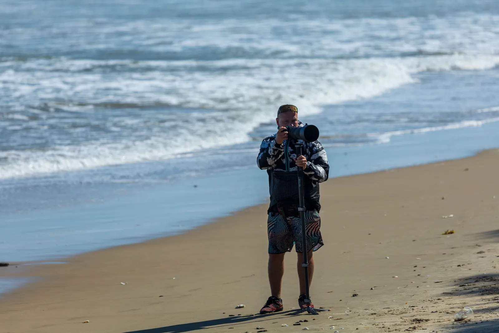 Photographer using a large camera on tripod capturing coastal waves on a sunny beach day
