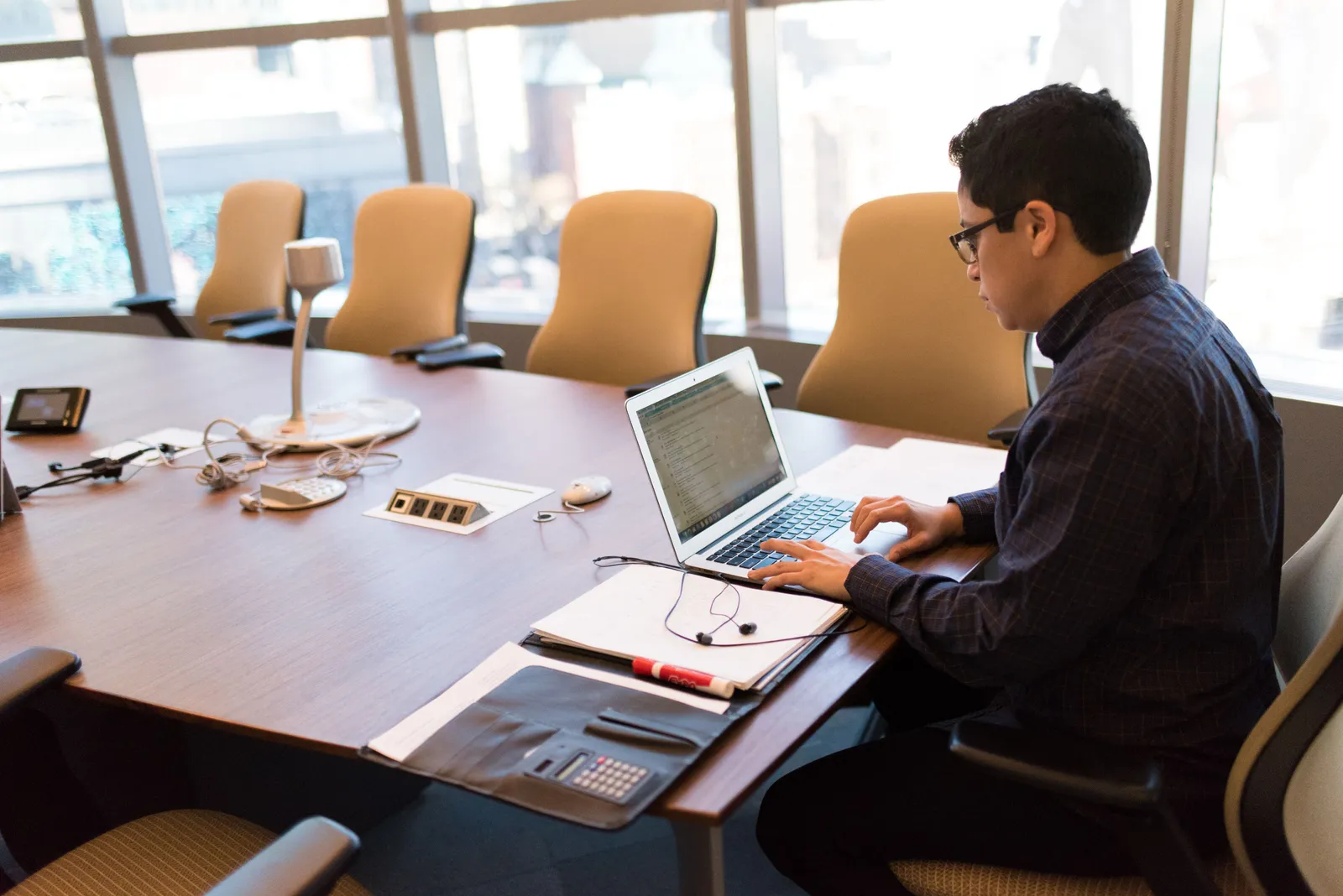 A professional adult sitting at a desk with a laptop in a bright, modern conference room