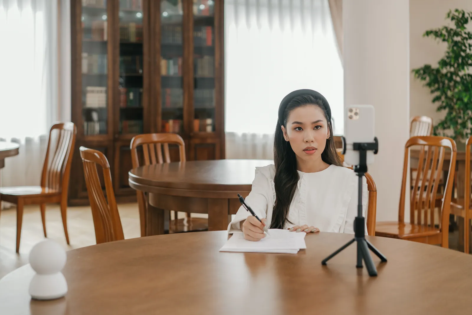 Young woman vlogging in a cozy home office setup using a smartphone and tripod