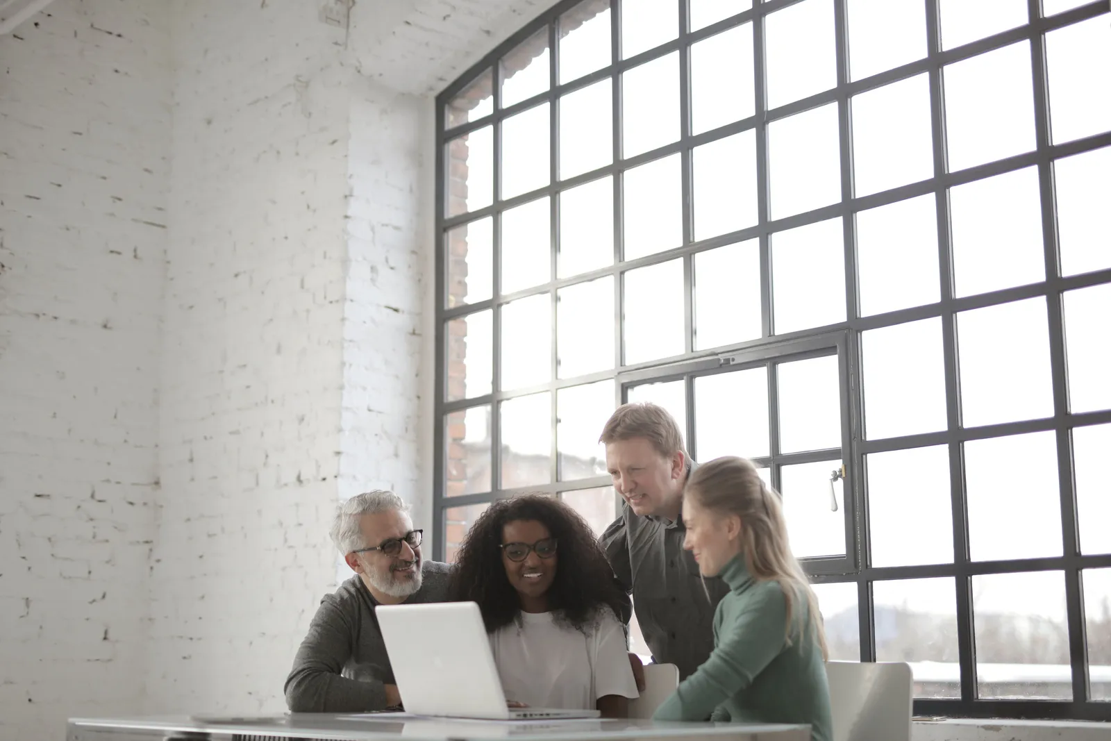 Positive focused multiracial coworkers gathering together near table with laptop in workplace at industrial building during
