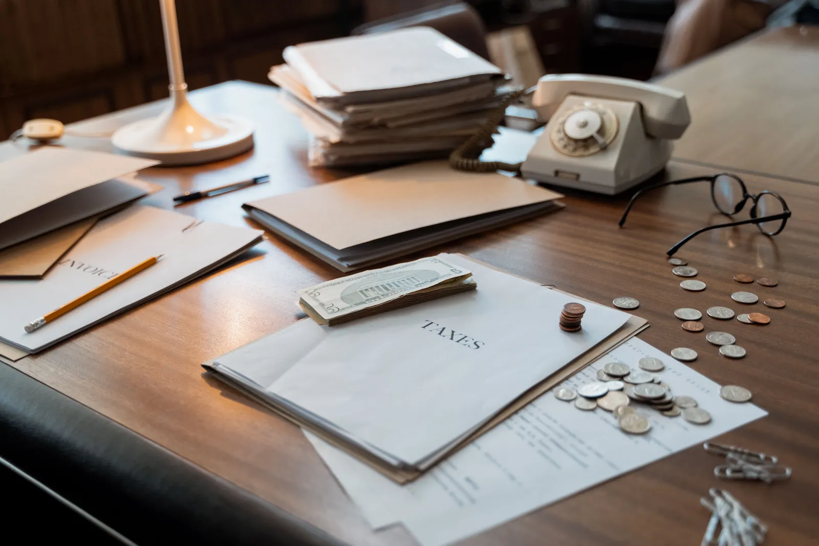 Close-up of an office desk with tax documents, coins, glasses, and an old phone, symbolizing finance and organization
