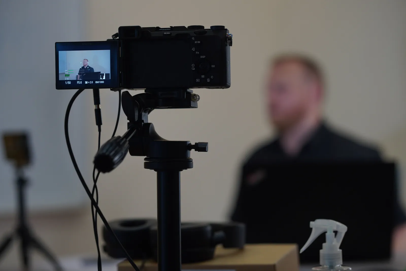 Close-up of camera setup during an indoor filming session with a blurred speaker in the background