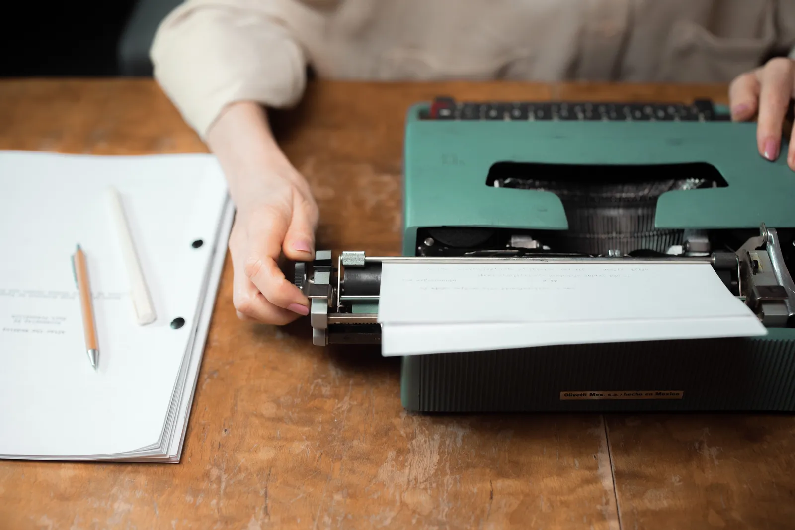 Close-up of hands typing on a vintage green typewriter with papers on a wooden desk