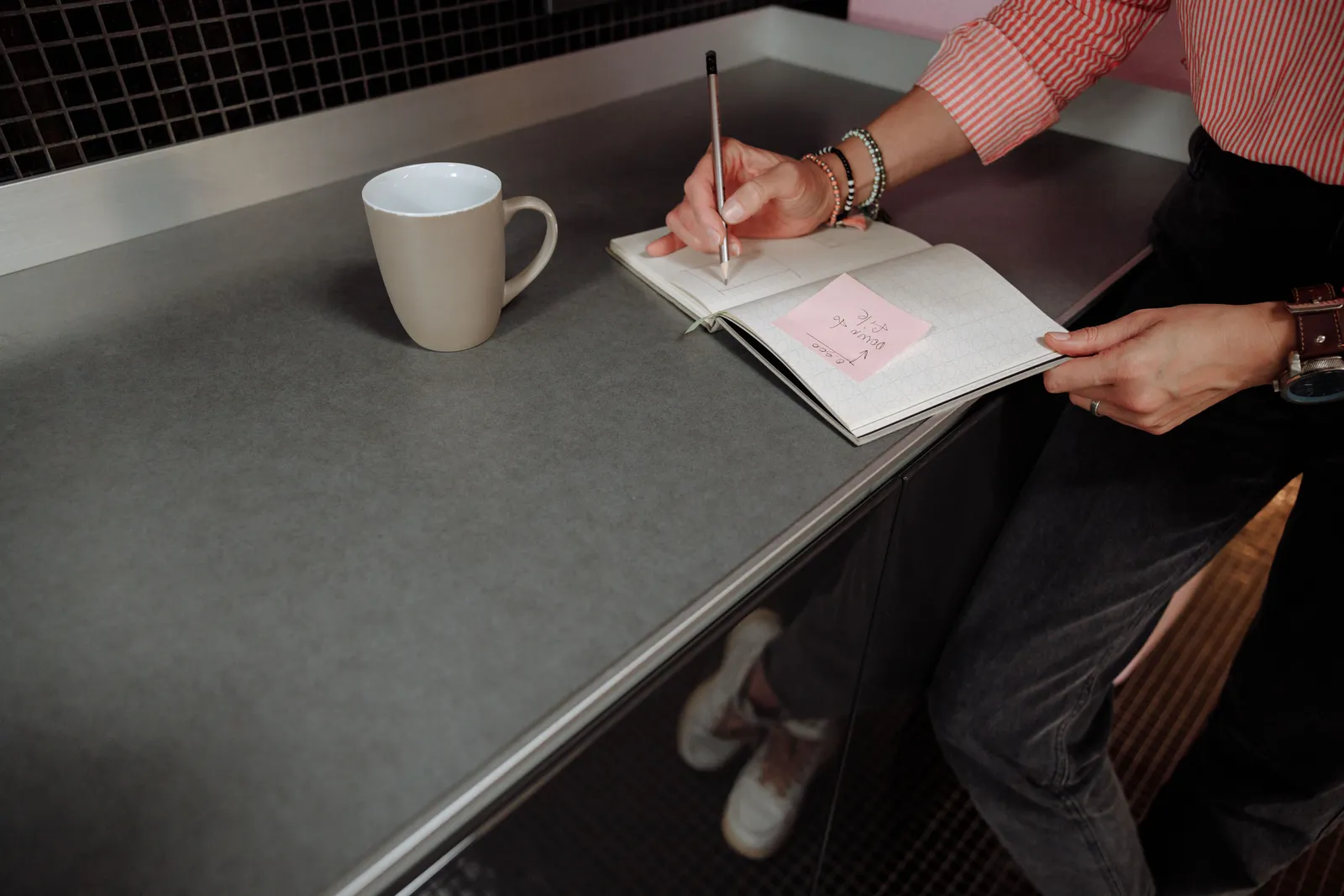 A person writing notes in a notebook with a coffee cup nearby on a desk