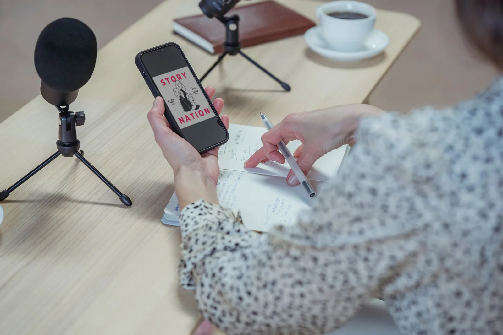 Back view faceless female in stylish blouse browsing mobile phone while sitting at desk with microphones and diary during