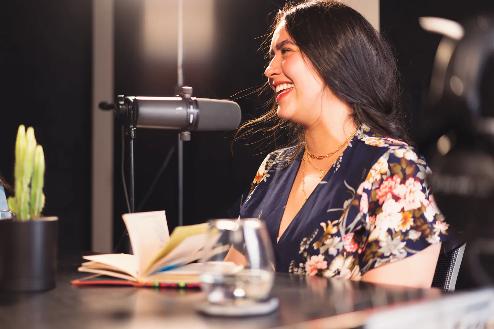 Woman in a vibrant studio setting recording a podcast with enthusiasm and expression