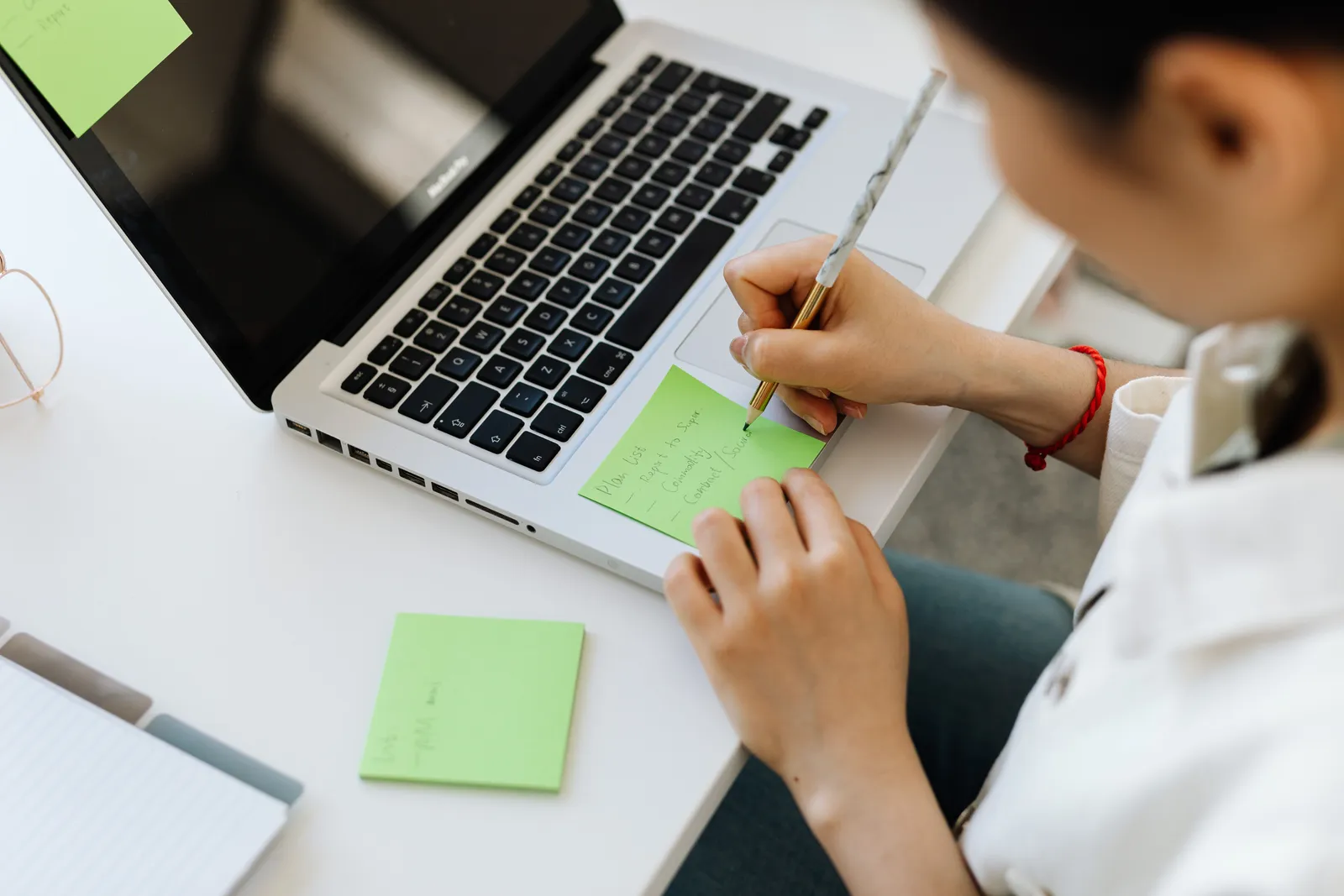 Person writing a to-do list on sticky note next to laptop for organization
