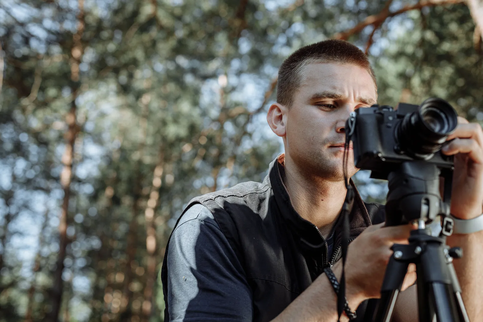 Focused photographer adjusting camera on tripod in a forest setting